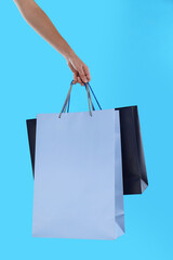 Woman with paper shopping bags on light blue background, closeup