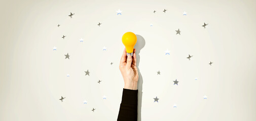 Fototapeta premium Person holding a yellow light bulb with silver shiny stars