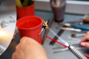 The artist heats the glass with a gas burner. The process of making glass jewelry. Master's hands close up