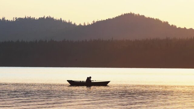 A silhouette of man sitting in a boat and fishing on nature while the sunset