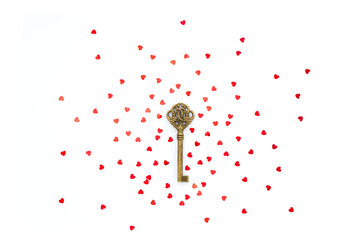 Old bronze key decorated with red hearts confetti on white background. The concept of the secret of love relationships.