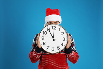 Man in Santa hat with clock on blue background. New Year countdown