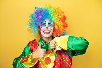 Clown standing over yellow insolated yellow background Doing thumbs up and down, disagreement and agreement expression. Crazy conflict