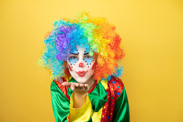 Clown standing over yellow insolated yellow background looking at the camera blowing a kiss with hand on air being lovely and sexy. Love expression.
