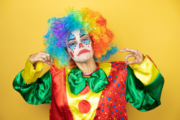 Obraz premium Clown standing over yellow insolated yellow background holding her t-shirt with a successful expression