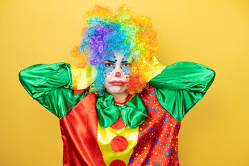 Clown standing over yellow insolated yellow background thinking looking tired and bored with hands on head