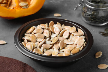 Full bowl of pumpkin seeds on grey table, closeup