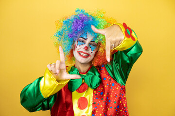 Clown standing over yellow insolated yellow background smiling making frame with hands and fingers with happy face