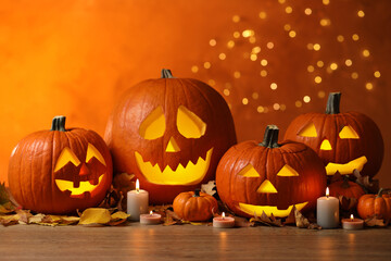 Pumpkin jack o'lanterns, autumn leaves and candles on table against blurred background. Halloween decor