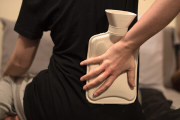 Una mujer sujetando una botella de agua caliente en su espalda