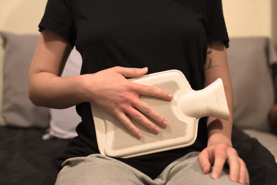 Una mujer sujetando una botella de agua caliente en su est&oacute;mago