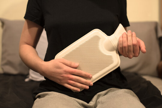Una mujer sujetando una botella de agua caliente en su est&oacute;mago