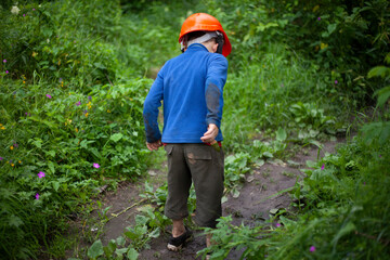 Child in the forest in an orange construction helmet. The boy's walk in an unknown place. Lost child in the mountains. The tourists forgot the boy.