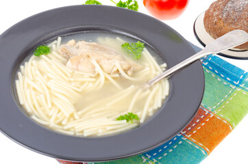 Chicken stock with slice of meat and noodles in black plate.