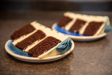 A rich moist chocolate cream three-layer cake with thick vanilla icing and greyish blue colored buttercream rosettes. The birthday cake is on a bright aqua blue ceramic dish sitting on a brown table.
