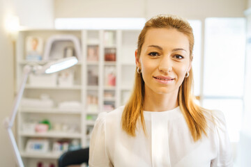 Front view on adult caucasian woman beautician doctor at spa - female professional cosmetologist standing at work in salon in day - healthcare and beauty concept