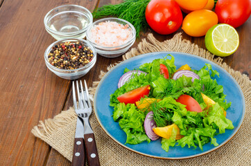 Light meal of green leaves of lettuce, yellow and red tomatoes, olive oil on wooden table.