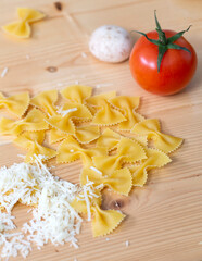 Butterfly shape macaroni and ingredients for cooking on wooden table