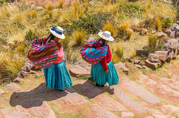 Fototapeta premium Two Quechua indigenous women in traditional clothing and textile walking down steps, Taquile island, Titicaca Lake, Puno, Peru.