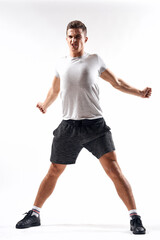A sports man in shorts and a full-length T-shirt does exercises on a light background
