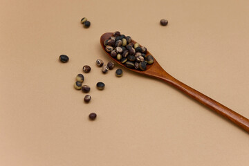 Black soybeans with wooden spoon on brown background.