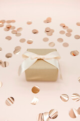 Mini gift box with pink satin fabric ribbon and rose gold confetti on pink background.
