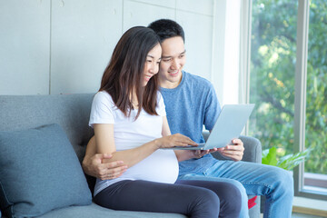 An expectant mother and father are sitting in the living room with a laptop computer..