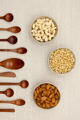 Various nuts (Pine nuts, almonds and cashew nuts) and wooden spoons and butter knife in a line.