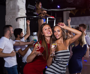 .smiling women dancing in the night club with drinks in the hand