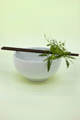 Chopsticks and green leaf on a white bowl.