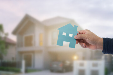 Hand holding paper house shape at house blurred background. House buy concept 