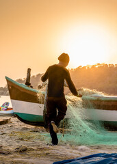 Fisherman collecting nets on the sandy shore of the Indian ocean at sunset