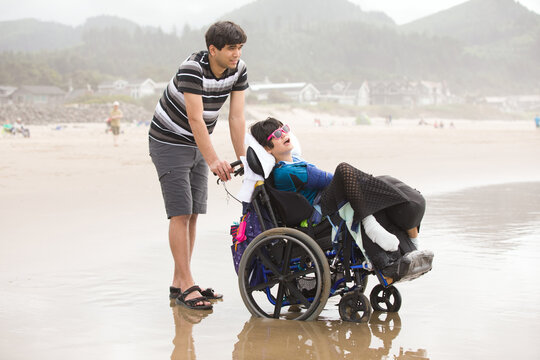 Young man pushing disabled little boy in wheelchair on beach