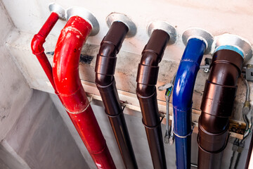 Different types of metal water pipes distinguished by colors connected to white concrete wall of a building.
Close up of a red, brown and blue pipes.