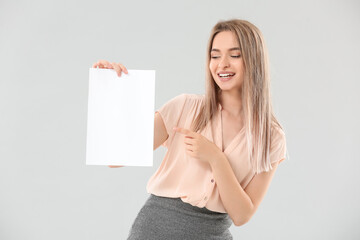 Naklejka premium Young woman with blank paper sheet on light background