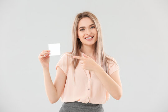 Young woman with small blank paper sheet on light background