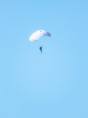 one parachutist floats slowly at low altitude on the background of clear sky