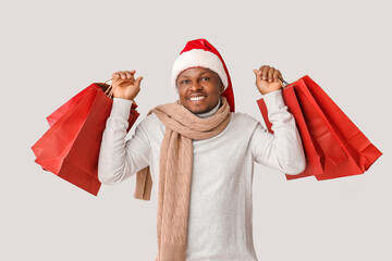 African-American man in Santa hat and with shopping bags on light background