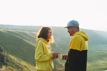 Obraz na płótnie Canvas Young happy family couple travelers in casual outfits with tea in morning on beautiful view background. Local tourism, the weekend trip