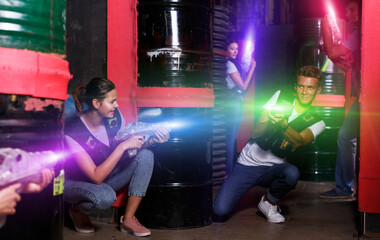 Group portrait of young smiling people with laser guns having fun together in dark labyrinth