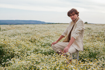 Tall handsome man sitting on a back of a chair in camomile flowers field