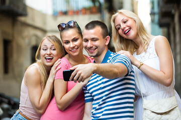Fototapeta premium portrait of four cheerful smiling young friends taking self picture using mobile phone outdoors . Focus on man.