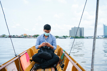 Business man wear mask travel by a boat in Bangkok.