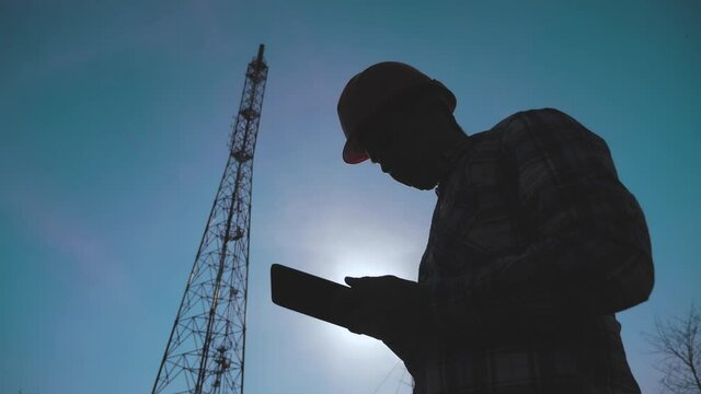 silhouette engineer man a studying telecommunication tower pillars. concept internet technology tv internet. hard hat worker lifestyle with digital tablet works in the information zone