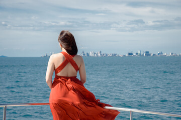 The scenery of a lone woman in red dress on yacht cruise looking to the city that far away in Pattaya bay, Thailand.