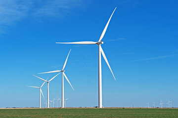 A row of windmills has been installed in a green field and is silhouetted against a blue sky.