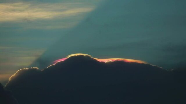 Iridescent pileus cloud on top of dark cloud is rare phenomenon on sky