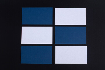Blue and white blanks glossy textured stack of business cards on black paper background, as template for design presentation.