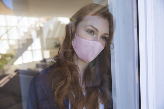 Woman wearing face mask looking out of the window at home