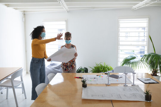 Two woman wearing face mask discussing over a blue print document at office - Powered by Adobe